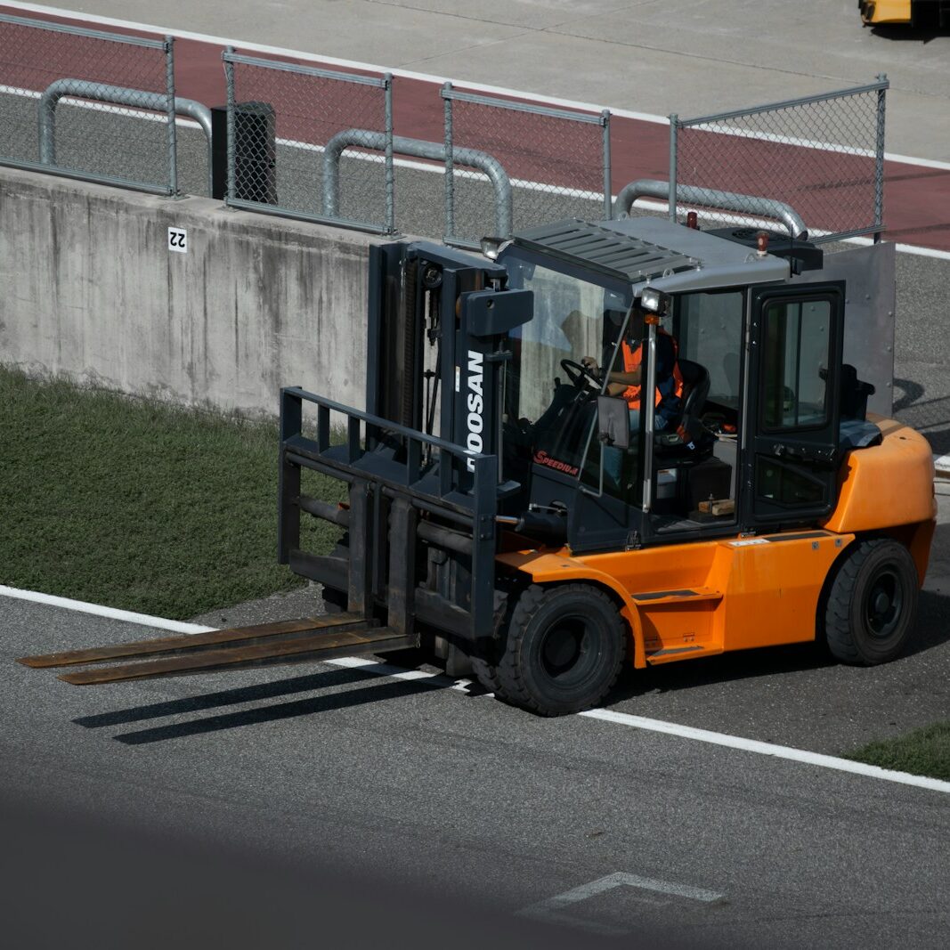 a forklift driving down a road next to a fence